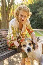 Elderly woman sitting on a park bench, gently petting her mixed breed dog while enjoying a tranquil
