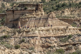 Group of hikers at colorful sandstone rock formations, desert, along gravel road Ruta Jubierre,