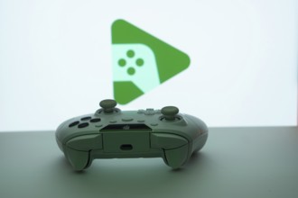 A close-up of a gamepad with the Google Play Games seen on screen in the background