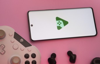 Smartphone with Google Play Games logo, game controller, and earbuds on a pink background