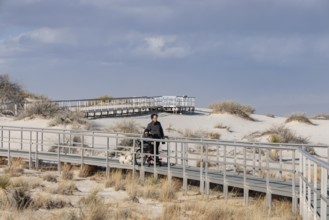 Man and handicapped woman in wheelchair stroll down the Interdune Boardwalk with their ped dog at