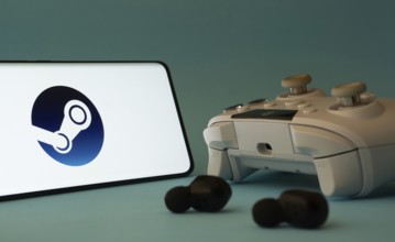 A smartphone with a Steam app icon next to a controller and earbuds on a blue surface