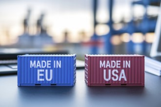Trade war concept. Small cargo shipping containers with text Made in EU and Made in USA with blurry