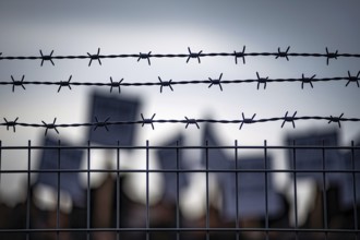 Barbed wire fence with blurred protesters and signs in background during border or prison