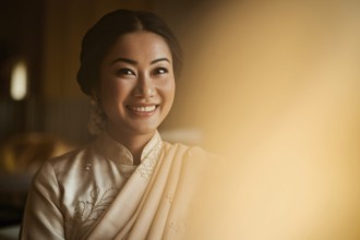 Smiling Thai woman in elegant traditional cream-colored outfit under warm golden light. Generative