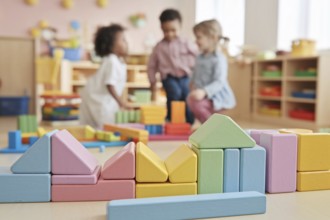 Pastel colored building bricks in sharp focus with children playing in the background, capturing