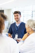 Young male nurse smiling and taking notes while talking with medical team in a hospital hallway