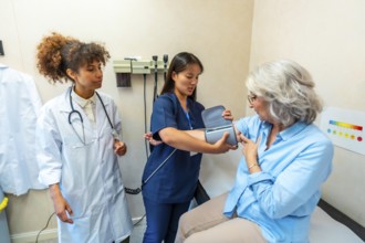 Nurse taking blood pressure of elderly woman during medical check up, supervised by doctor,