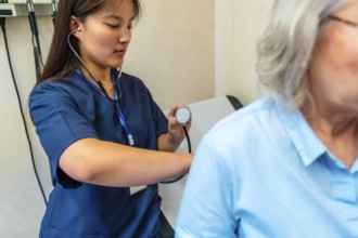 Female doctor using stethoscope examining lungs of senior patient during medical checkup in