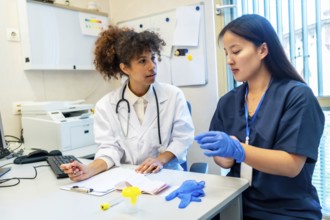 Doctor explaining medical procedure to a nurse wearing gloves, sitting at a desk in a hospital