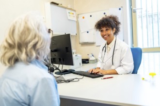 Smiling female doctor wearing lab coat and stethoscope typing on computer keyboard while listening