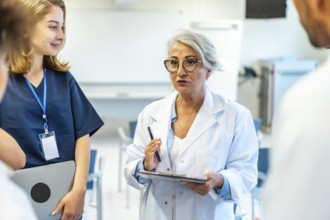 Experienced female doctor leading a medical briefing, holding a clipboard and pen, addressing