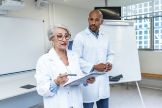 Senior female doctor explaining a healthcare project to colleagues, holding clipboard and pointing