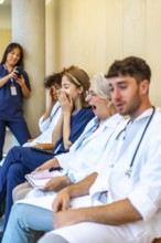 Exhausted doctors and nurses yawning while sitting in a hospital hallway, waiting for their next