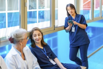 Asian nurse using a smartphone while colleagues chat and relax during a break in the hospital