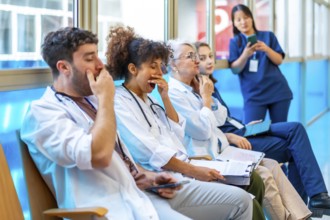 Exhausted medical professionals yawning while sitting on chairs in a hospital corridor,