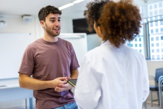 Young man holding a tablet, engaging in a conversation with a doctor inside a hospital room,