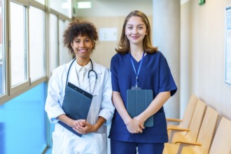 Doctor and nurse smiling while holding medical records in a hospital corridor, showcasing teamwork