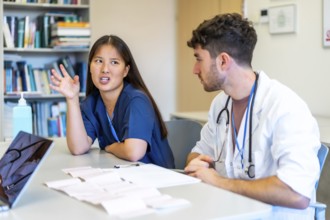 Two young doctors reviewing medical records and having a discussion about a patient chart at a