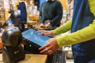 Salesperson using a touch screen cash register in an organic supermarket, selling natural and