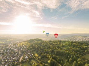 Hot air balloons float over a hilly and wooded landscape at sunset, Calw, Black Forest, Germany