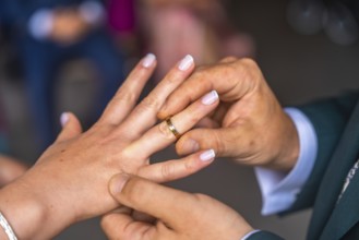 Groom gently placing golden wedding ring on bride's finger during wedding ceremony, symbolizing