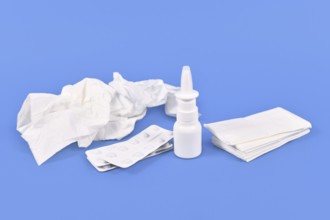 Nasal spray bottle, medicine pills and used tissues used during common cold on blue background