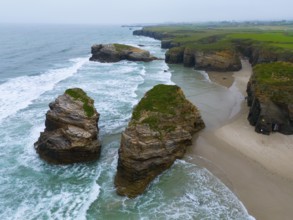 Gigantic, jagged rocks jutting out of the sea and lapped by foaming water, aerial view, Praia das