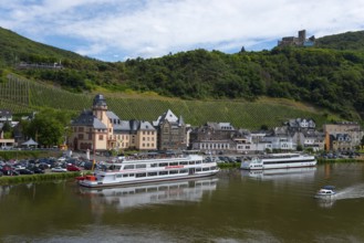 River landscape with anchored ships on the banks, surrounded by vineyards and historic buildings,
