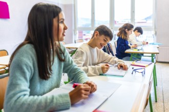Smiling elementary school students writing on their notebooks during class, learning and education
