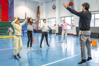 Students and teacher performing jumping jacks during physical education class in school gymnasium,