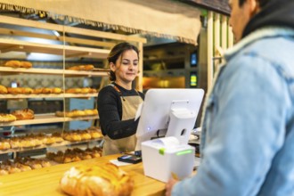 Rear view of a latin young man checking out in an artisan bakery attended by a latin young