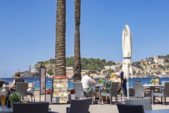 People sitting on a restaurant by the sea at a coast village at a tourist resort, Port de Sóller,