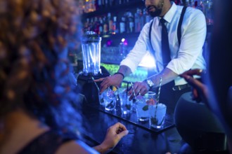 Professional bartender preparing cocktails at bar counter in nightclub, using fresh ingredients and
