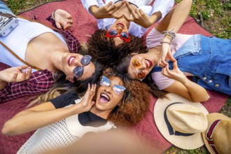 Four multi ethnic female friends are lying in circle on blanket in a park, making heart shape with