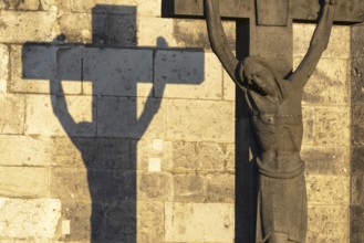 Stone cross with shadow cast at sunrise, cathedral cemetery near Cologne Cathedral, Cologne, North