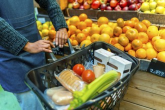 Supermarket employee pushing a shopping cart full of fresh produce, packaged goods, and vegetables