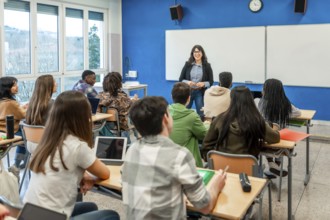 Female teacher explaining lesson to attentive multi ethnic high school students sitting at desks