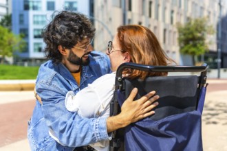 Smiling man hugging a happy woman sitting in a wheelchair in a city park, enjoying a sunny day
