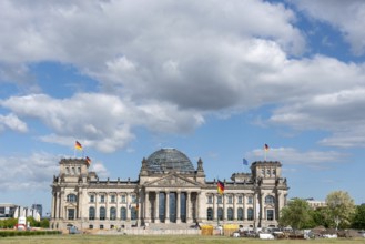 Front view of the Reichstag under a cloudy sky with waving flags, Berlin, Germany