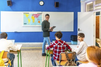 Geography teacher walking in classroom while students are studying with laptops and books