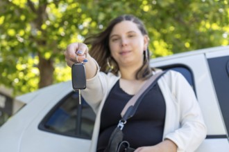 Proud businesswoman holding car keys in front of her new electric car, smiling with satisfaction