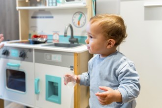 Curious toddler holding a glass while playing with toy kitchen set, exploring and learning through