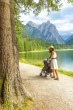 Tourist enjoying a walk with a baby stroller along the scenic shores of lake dobbiaco, surrounded