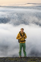 Young man in front of impressive landscape at sunset, fog, clouds moving around, glacier ice of the