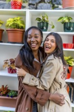 Two female shop assistants laughing and hugging each other in a plant shop, celebrating their