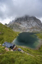 Alpenverinshütte Wolayerseehütte on Lake Wolayersee, cloudy mountain landscape with green meadows