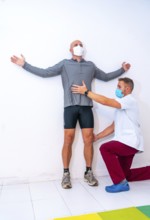 Physiotherapist with mask stretching client's neck with a hair on the wall. Physiotherapy with