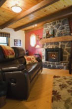 Lit wood burning dark grey natural stone fireplace and brown leather sofa in living room with