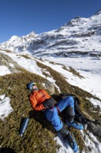 Ski tourer taking a break in the sun, lying down, taking a nap, snowy mountain landscape in winter,
